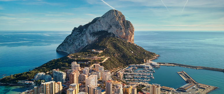 Panoramic view of Calpe's coastline with the iconic Peñón de Ifach under a clear blue sky.