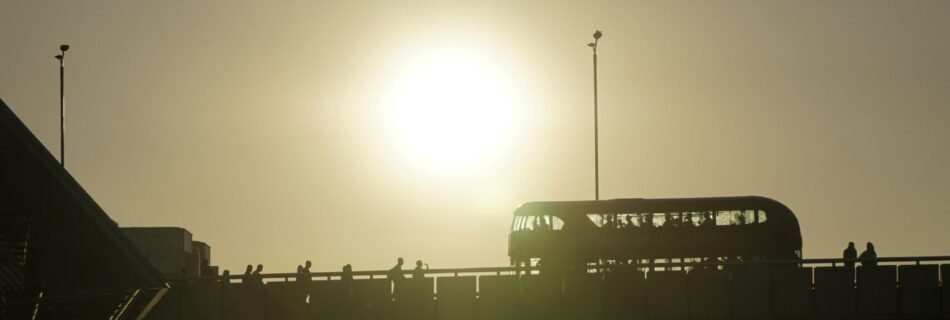 The sun is setting over a bridge with a bus on it