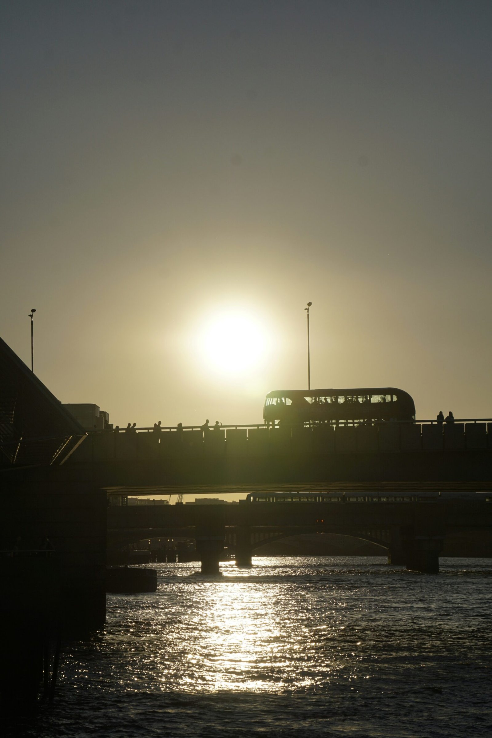 The sun is setting over a bridge with a bus on it