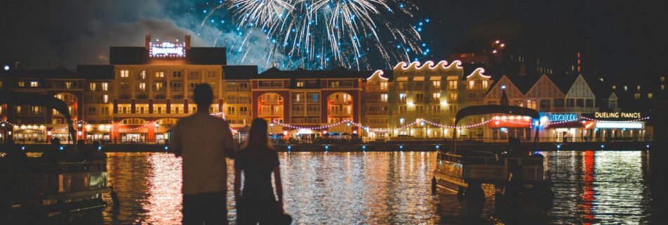 two people standing beside body of water watching fireworks