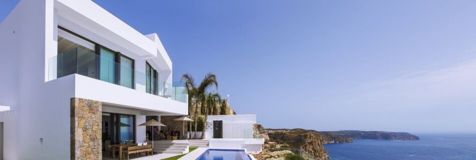 Modern luxury villa with a private pool and stunning sea views on a cliffside in Spain, featuring sleek white architecture and glass balconies.