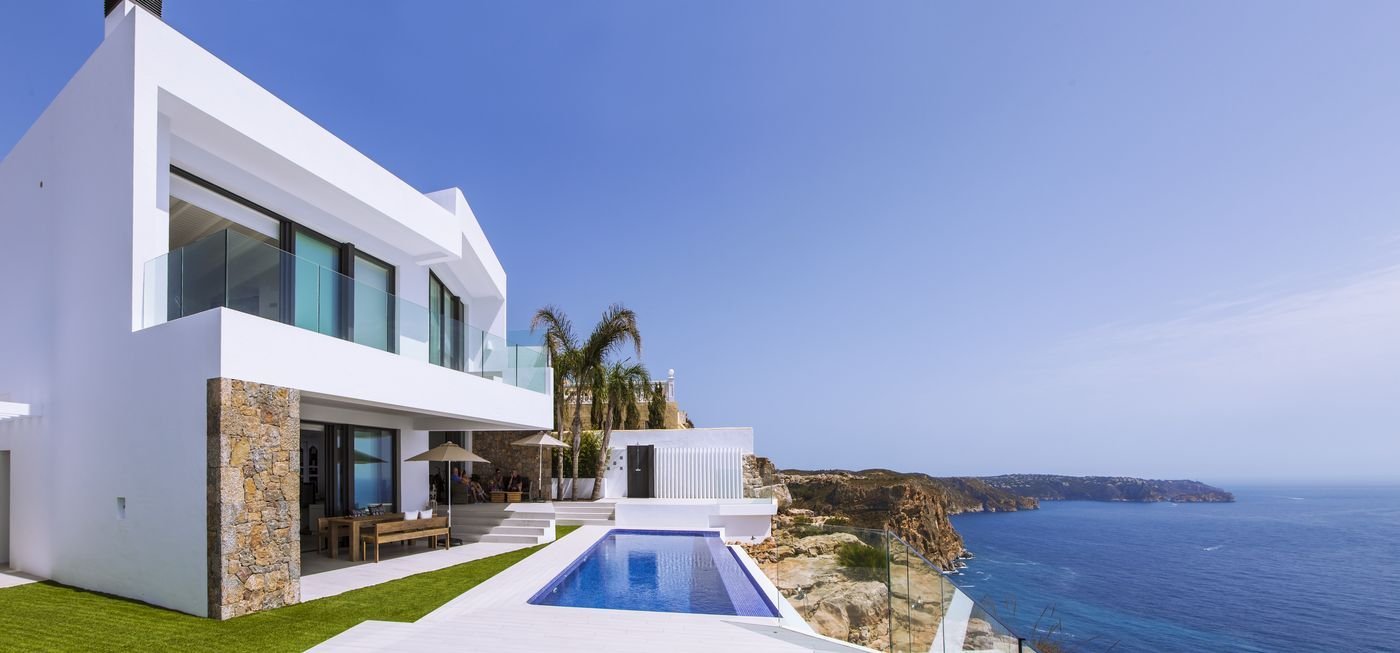 Modern luxury villa with a private pool and stunning sea views on a cliffside in Spain, featuring sleek white architecture and glass balconies.