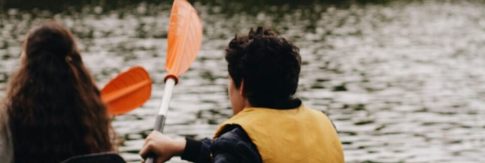 woman in yellow and black jacket riding green kayak on lake during daytime